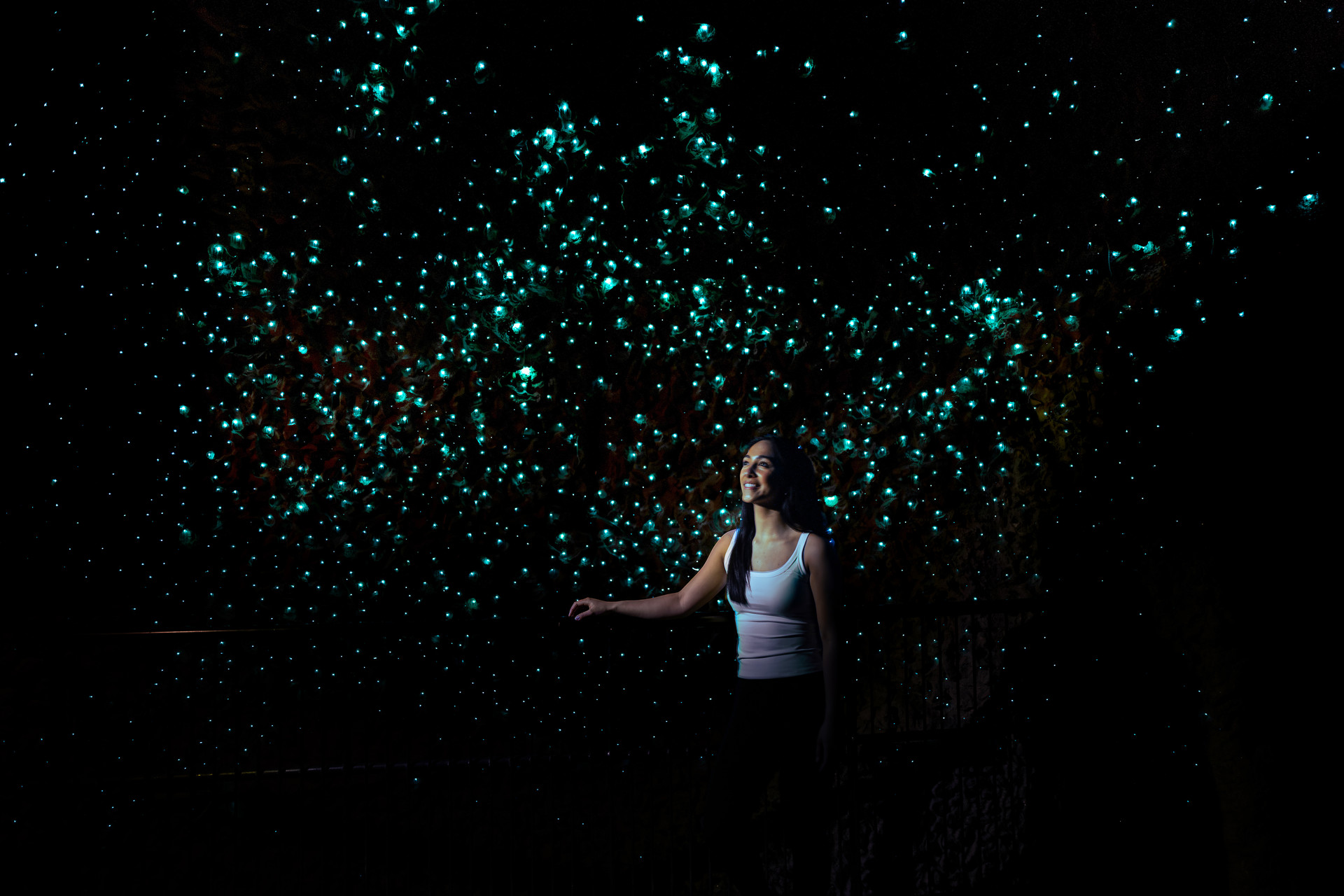 Visitor smiling beneath a ceiling of glowing blue-green glowworms